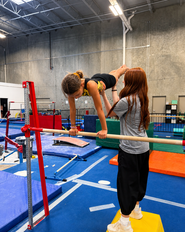 Coach spotting a gymnast on the uneven bars at High Altitude Tumbling