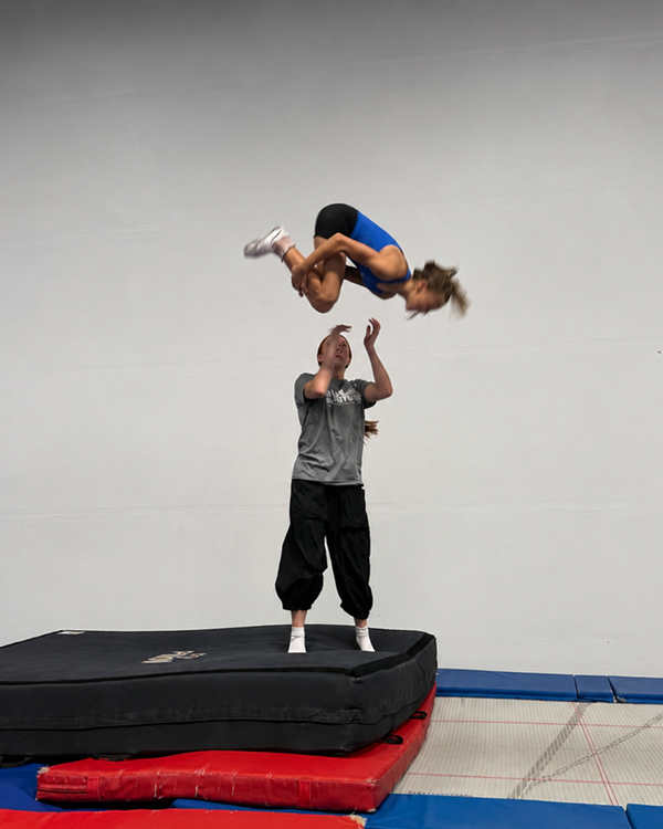 Coach tossing and catching an athlete mid-flip